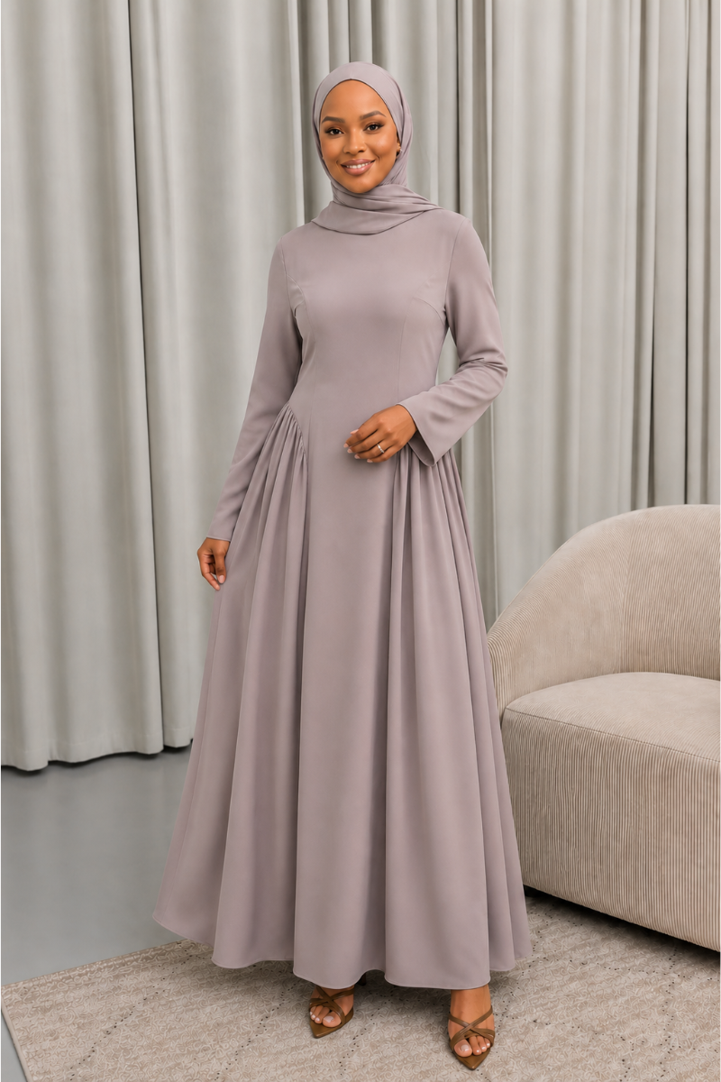 Veiled Muslim woman wearing a hijab in The Aura Dress, a full-length modest maxi dress with long sleeves, crew neckline, gathered pleated waist and flowing skirt