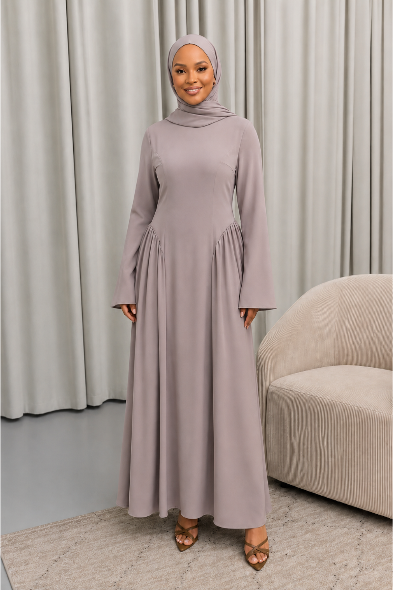 Veiled Muslim woman wearing a hijab in The Aura Dress, a full-length modest maxi dress with long sleeves, crew neckline, gathered pleated waist and flowing skirt