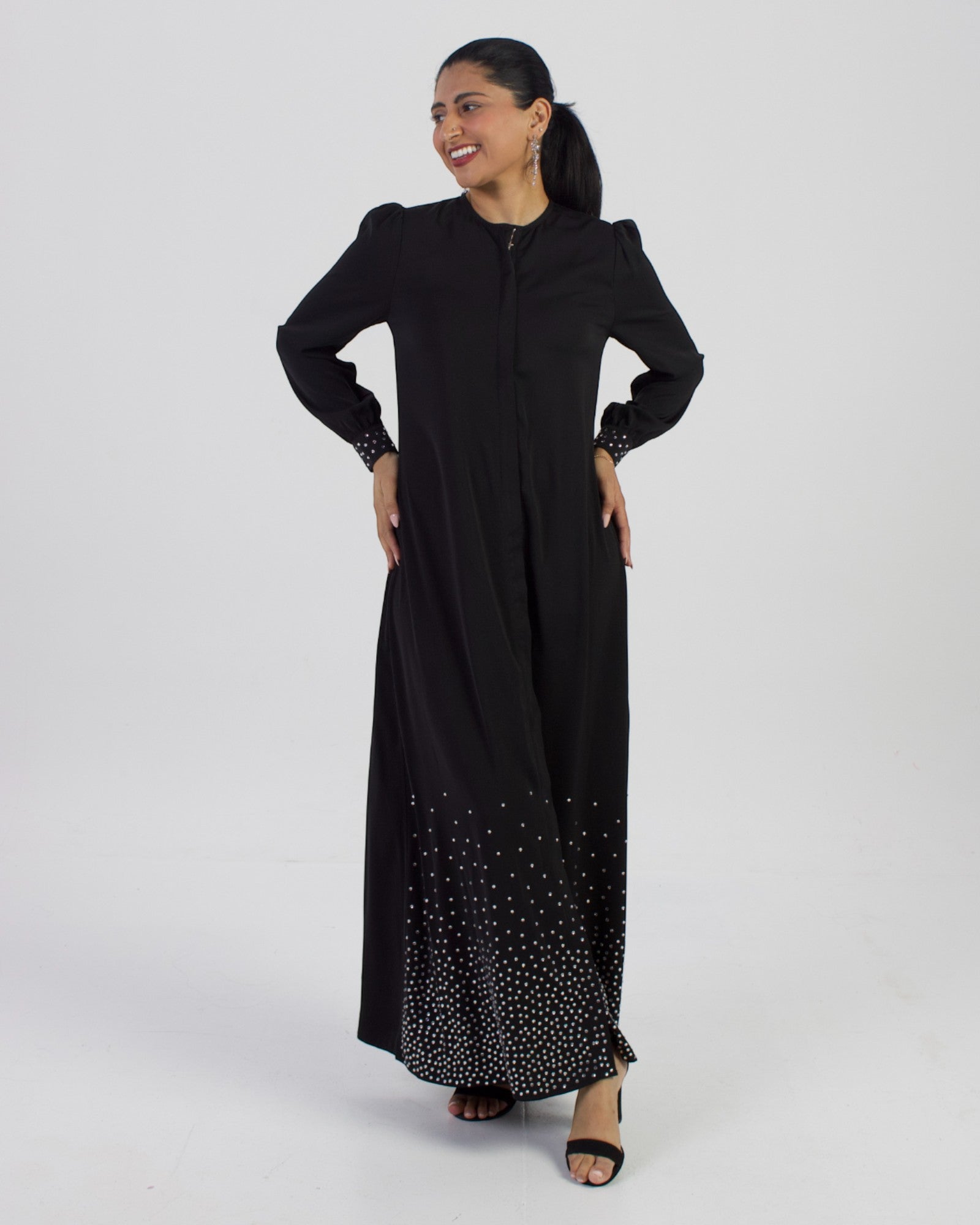 Model in Midnight Majesty studded long sleeve black abaya dress with silver embellishments on cuffs and hem.
